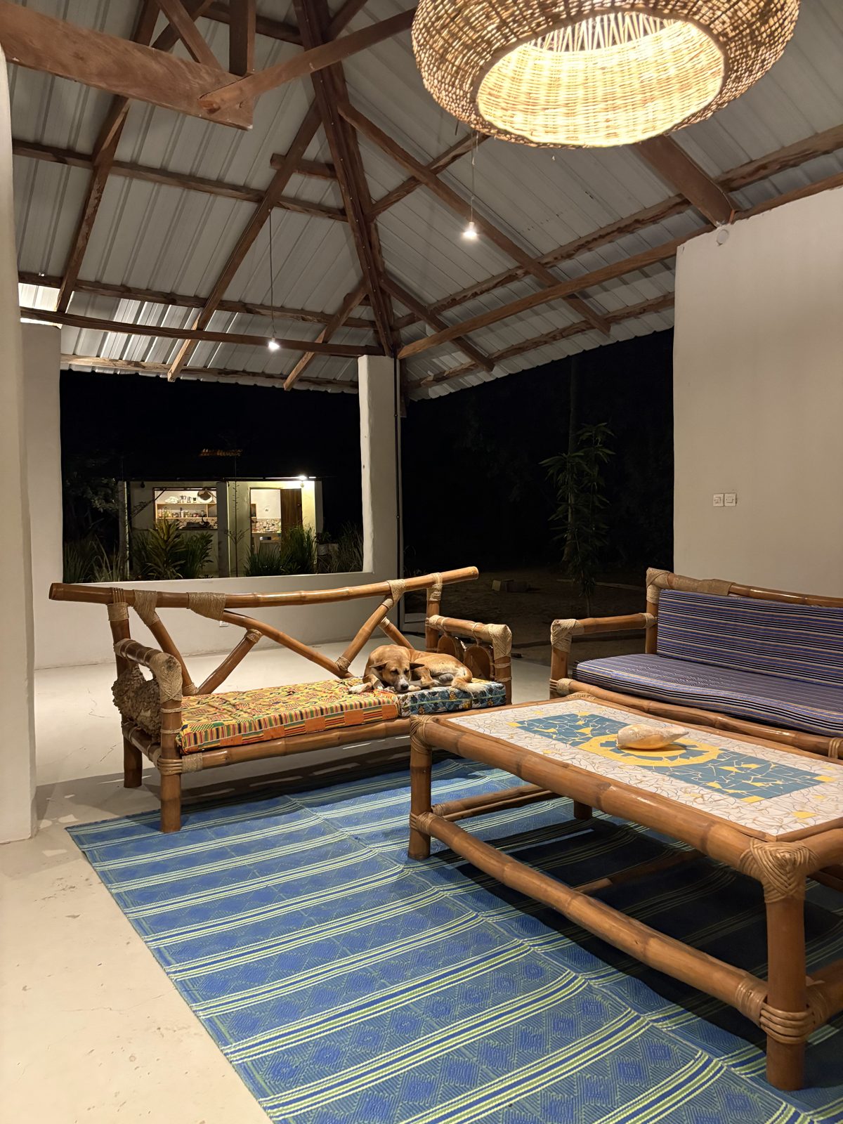 The finished main room of the school at night, with bamboo sofas, a mosaic table and a woven lamp under the new roof