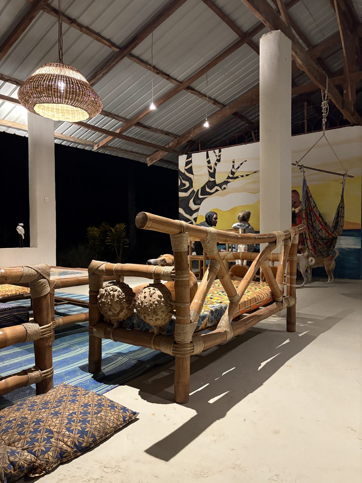 A bamboo sofa with a woven lamp and cushions in the school hall, a hammock in the background