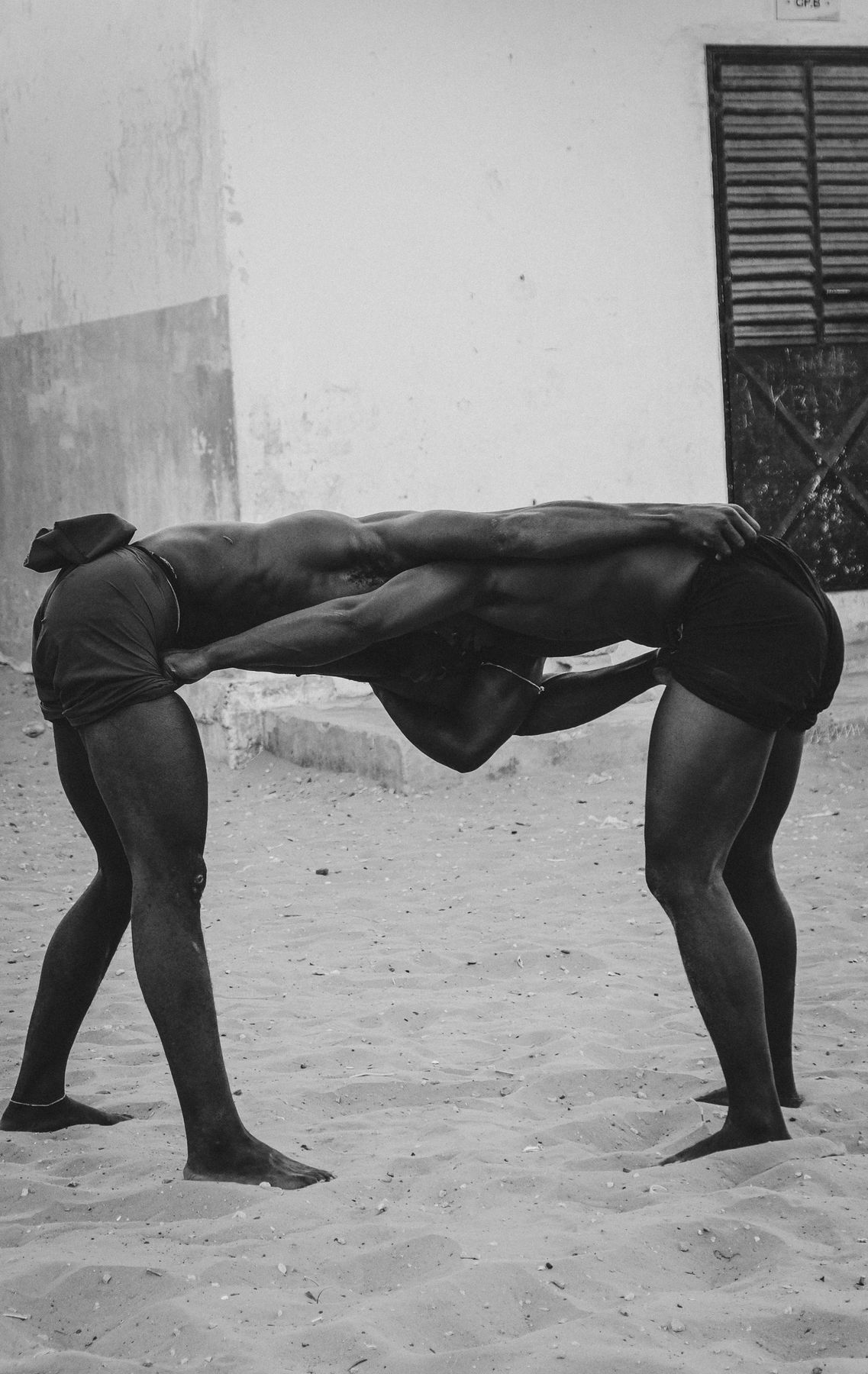 Two wrestlers bent over, gripping each other's shorts, in front of a white wall