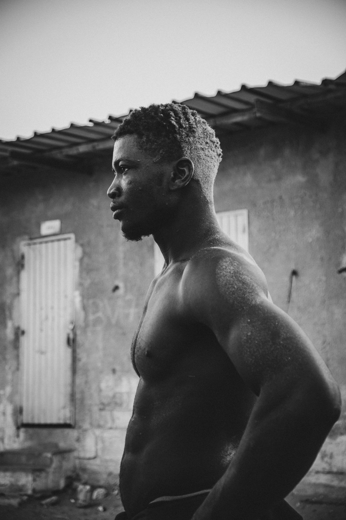 Profile of a wrestler in front of a worn wall, sweat on his shoulders